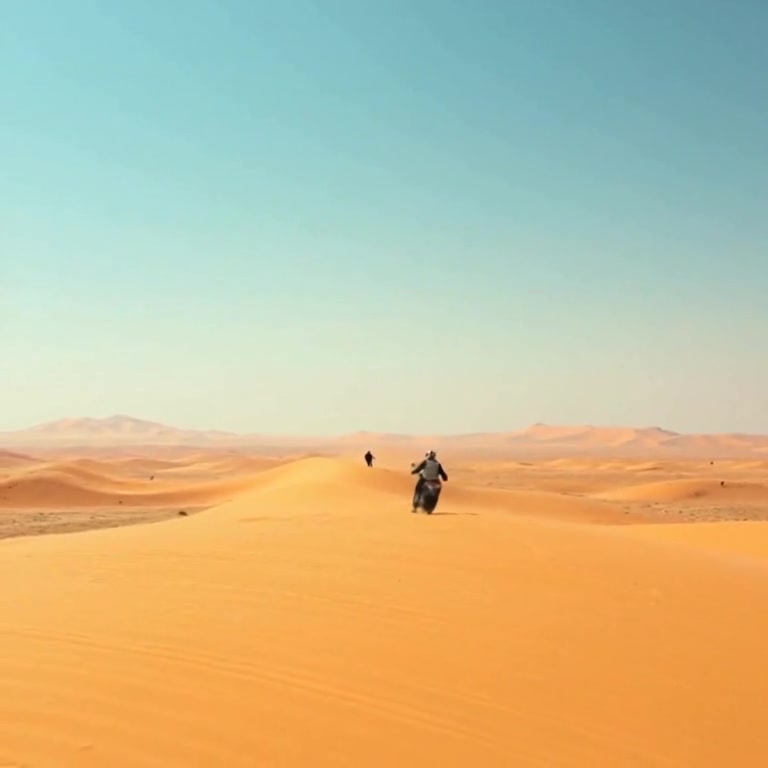 Gentle winds ripple the surface of the golden sand dunes under a bright blue sky, creating flowing patterns across the landscape.