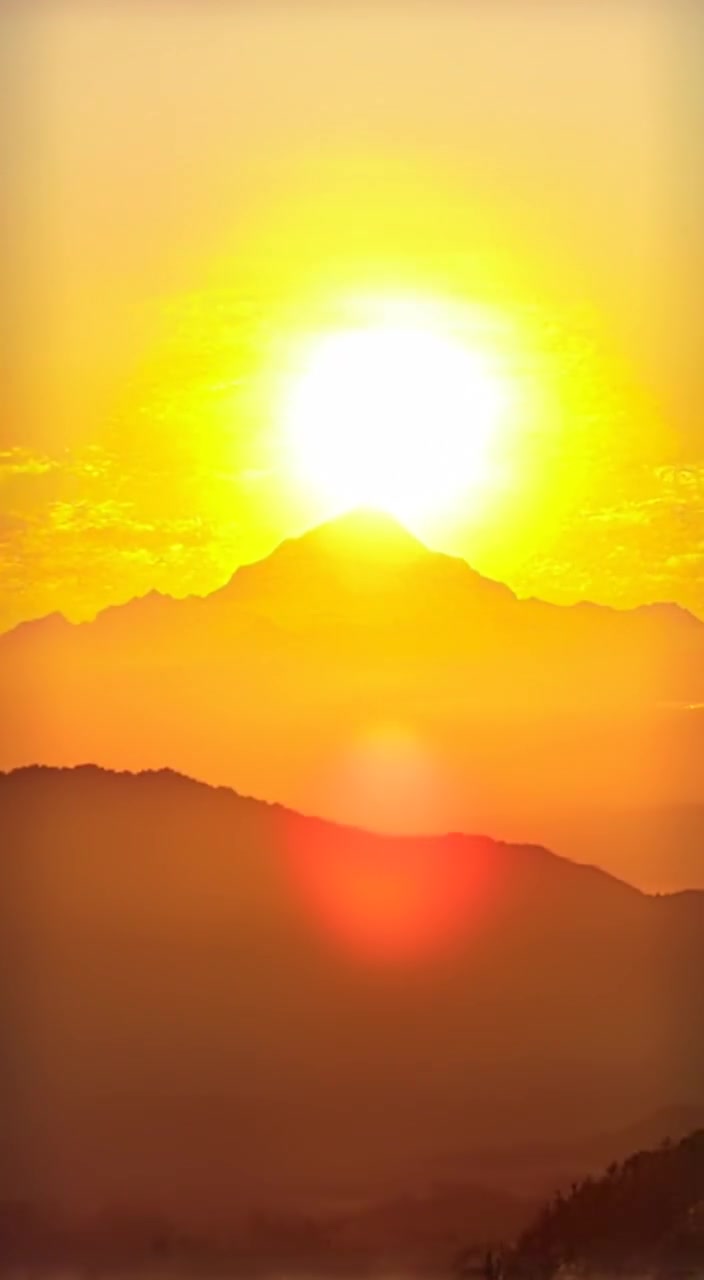 Golden and rose hues gently blend as the sun rises over the distant mountains.