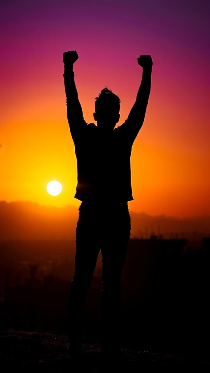 Subject: A young person standing confidently at the top of a hill. Subject movement: The individual raises their arms in triumph as the sun rises, the light illuminating their fierce expression. Scene: Overlooking a sprawling city skyline bathed in the warm glow of sunrise, with soft clouds catching the golden light. Motion: Camera pushes in from a wide shot to a close-up, capturing the person's determined expression against the breathtaking backdrop, with ambient morning light creating an uplifting atmosphere.