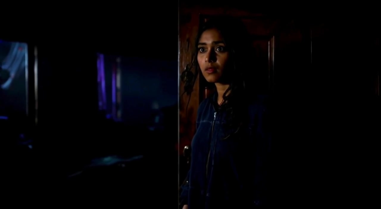 The woman takes a cautious step forward, her eyes scanning the dimly lit surroundings with a mix of fear and curiosity.
