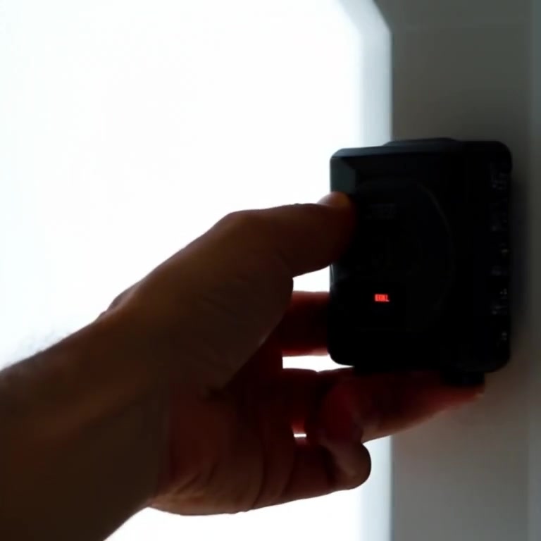 A hand gently presses the emergency call button against the clean white wall.