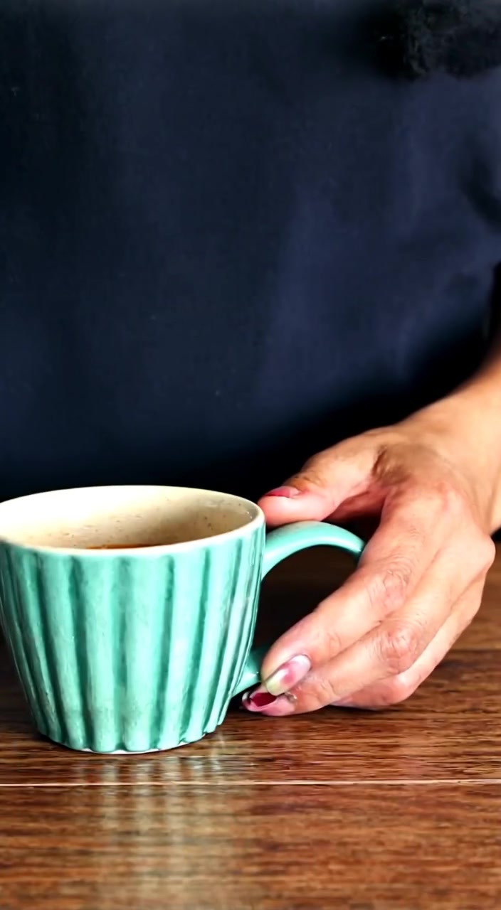 The woman gently pours freshly brewed coffee into a stylish mug on the wooden countertop.