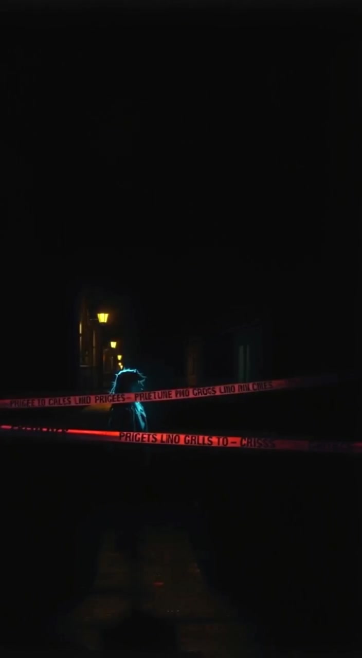 A flickering streetlamp casts shadows over police tape fluttering gently in the night breeze.