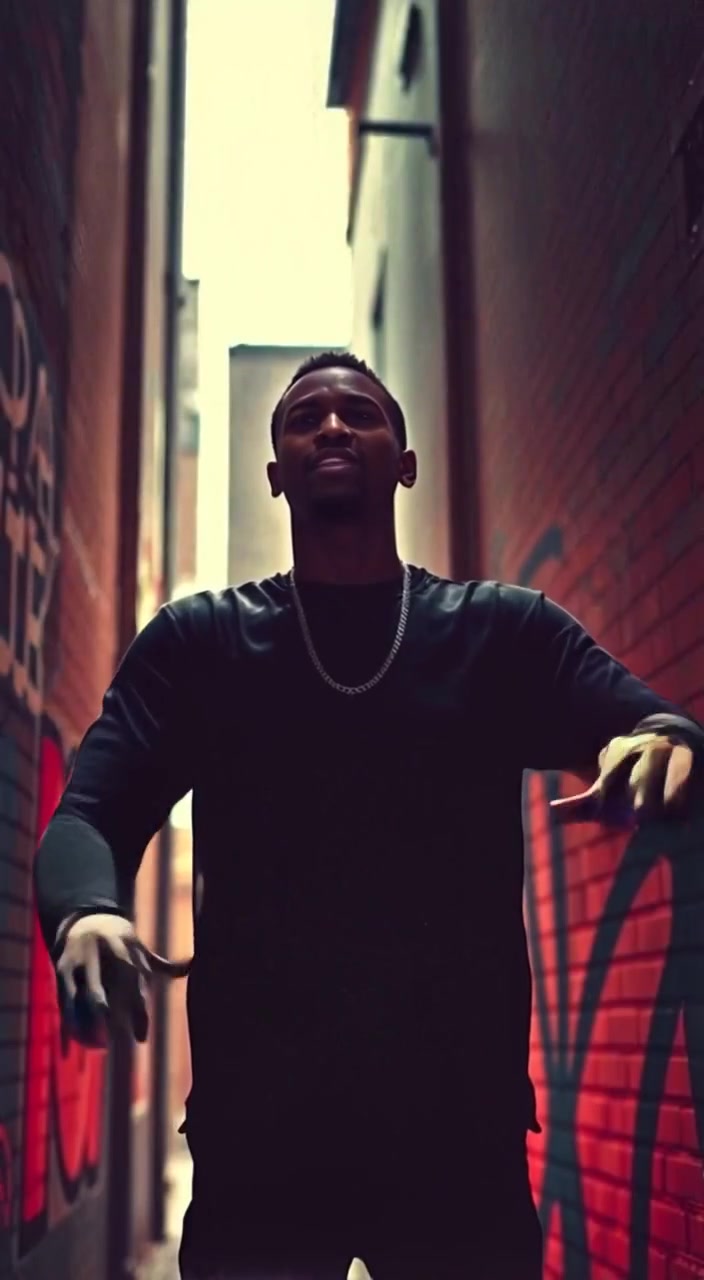 The man gestures expressively while rapping, with vibrant graffiti art on the alley walls behind him.