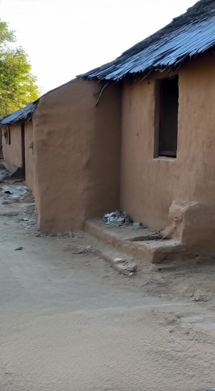 A woman gently carries water from the well towards her mud house in the warm afternoon sunlight.