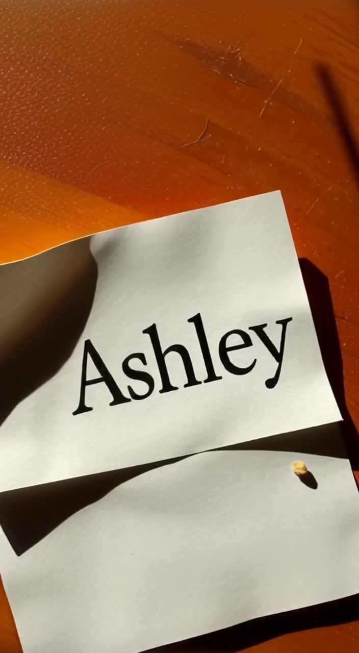 A gentle breeze unfurls the edges of a note resting on a wooden table, revealing the name 'Lila'.