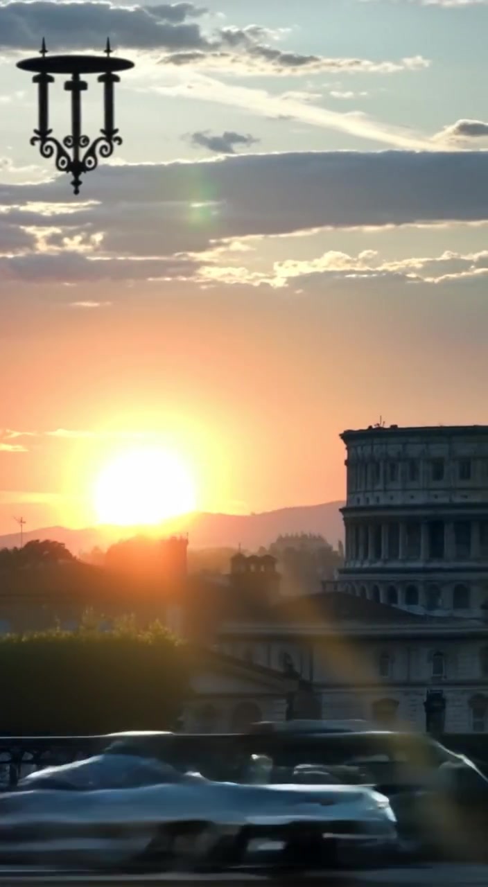 Soft light gradually brightens the skyline of Rome as the sun rises behind the Colosseum, casting gentle shadows.