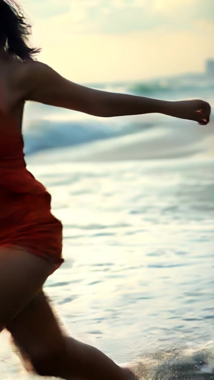 Subject: A young woman joyfully running along a beach. Subject movement: She dashes playfully, splashing through the waves that crash at her feet. Scene: A sunny beach with rolling waves and fine golden sand, framed by a clear blue sky. Style: Bright, invigorating daylight casts lively shadows on the beach. Motion: The camera employs a dynamic tracking shot, following her movement from a low angle, capturing the water splashing around her feet as she bounds along the shoreline.