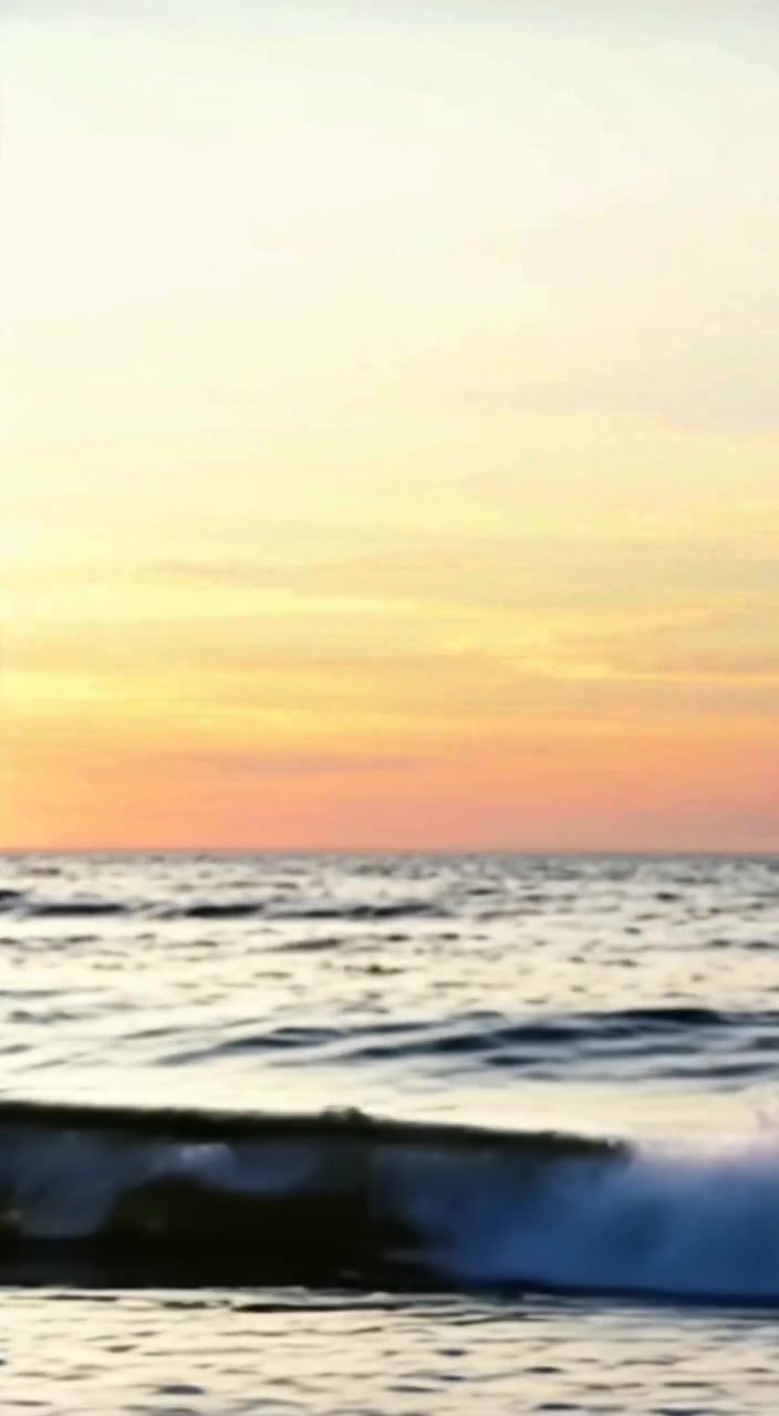 The boy watches waves gently crash on the shore, absorbed in thought as the tide rolls in.