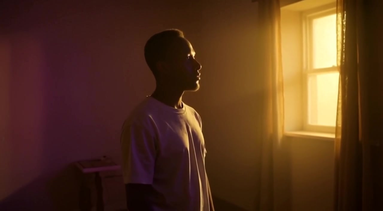 The figure slowly turns towards the brilliant light, their expression reflecting awe and curiosity in the dim room.