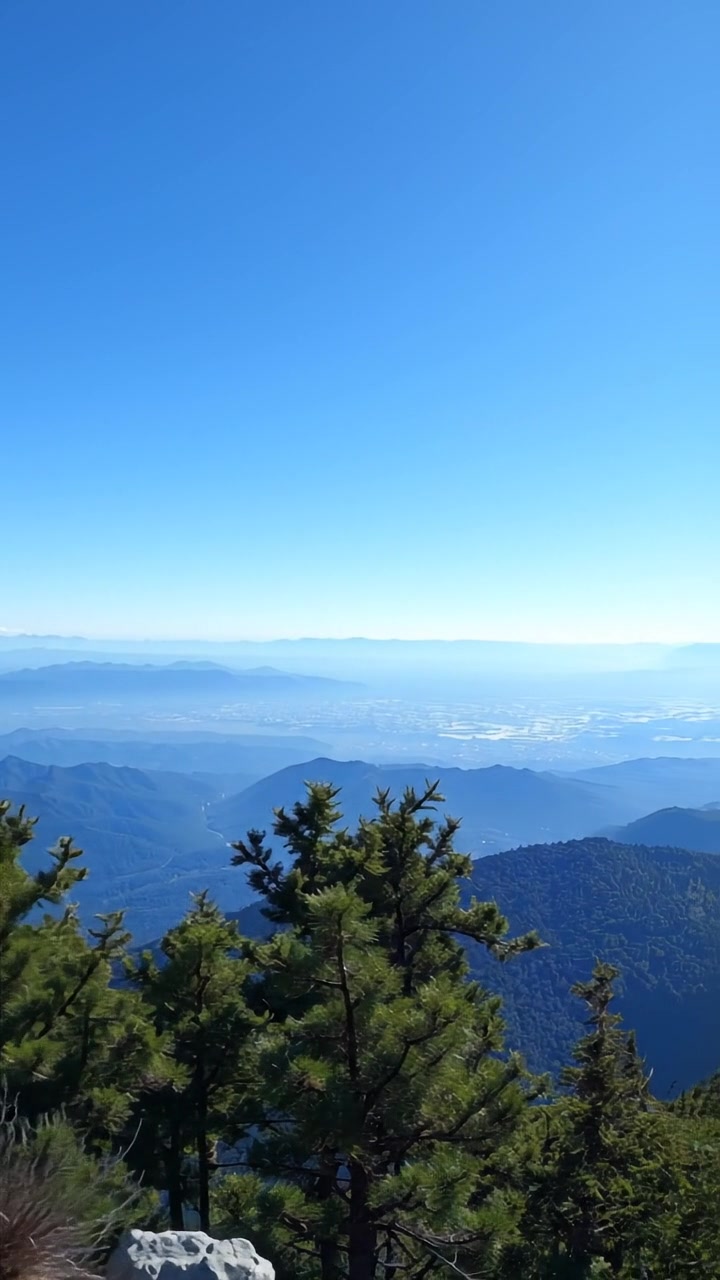 A panoramic view from a high vantage point showcasing distant mountain ranges, bathed in soft, natural lighting with high detail and smooth camera movement, emphasizing the vastness and rugged beauty of the landscape. The background features gentle mountain silhouettes under a clear sky. The audio features ambient nature sounds.