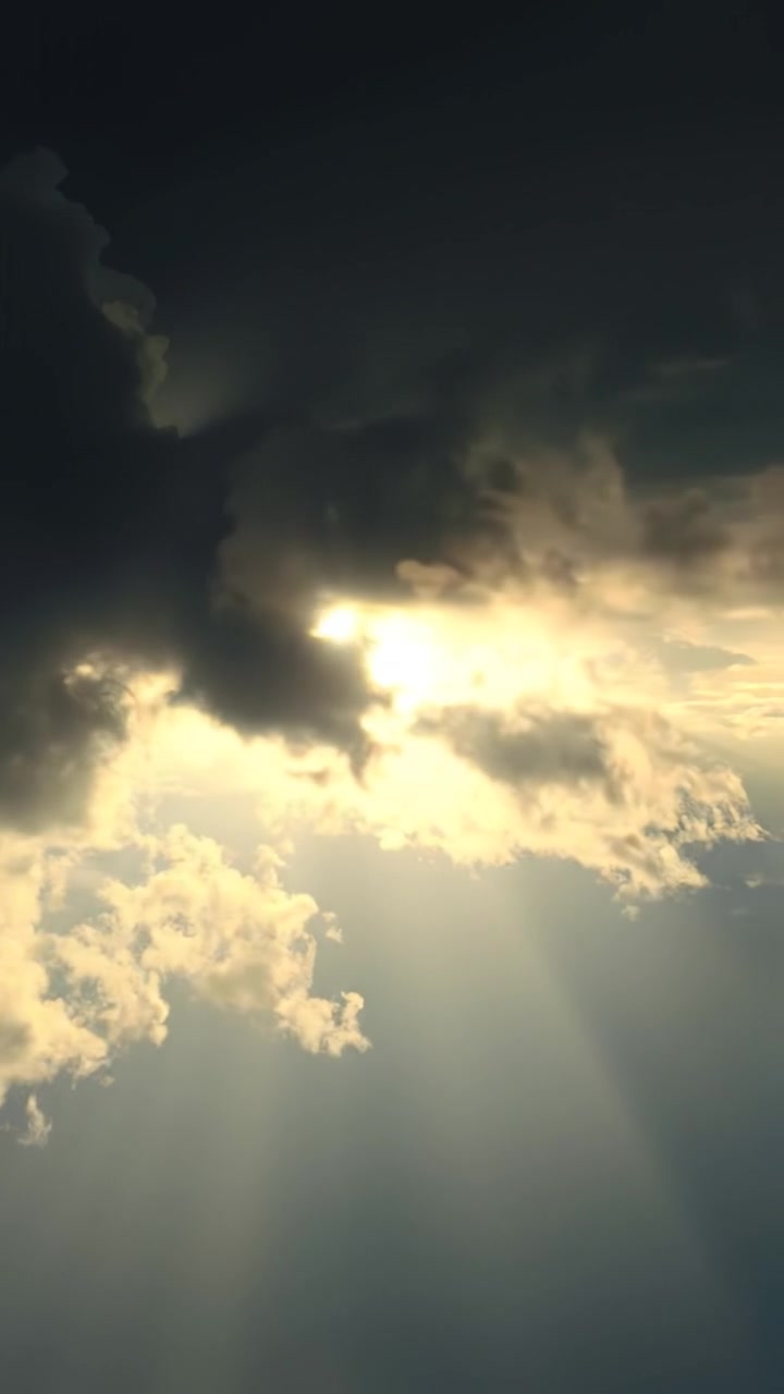 A radiant ray of light breaking through dark clouds, illuminated with warm, golden tones, detailed textures of the clouds visible, smooth camera dolly shot emphasizing the contrast, with soft ambient light creating a dramatic sky. The background audio features a gentle breeze and distant thunder.