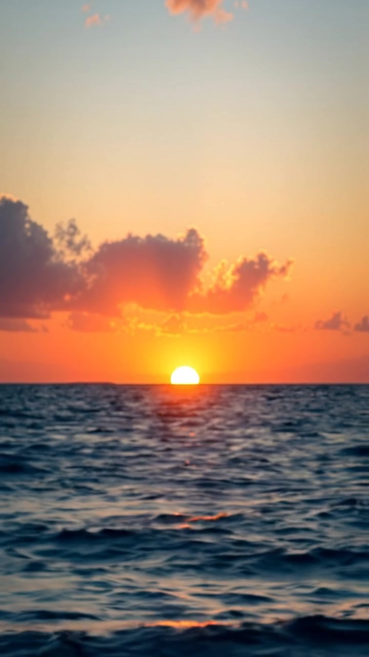 A breathtaking scenic view of the ocean at sunset, with vibrant warm tones casting a golden glow over the rolling waves, captured with smooth camera movement for cinematic elegance. The background features a serene horizon, gentle waves shimmering in the fading light, with soft ambient sounds of ocean waves in the background.