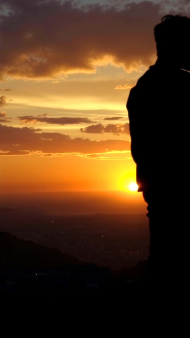 Scene: A silhouette of a figure standing on a hill at dawn, gazing over a distant city as the first light of day spills across the horizon. Style: Soft, pastel morning light gradually illuminating the landscape, creating a serene and hopeful atmosphere. Motion: The camera slowly pushes in from a wide angle to capture the vastness of the cityscape below, enhancing the sense of contemplation as the sky gradually brightens, revealing vibrant hues.
