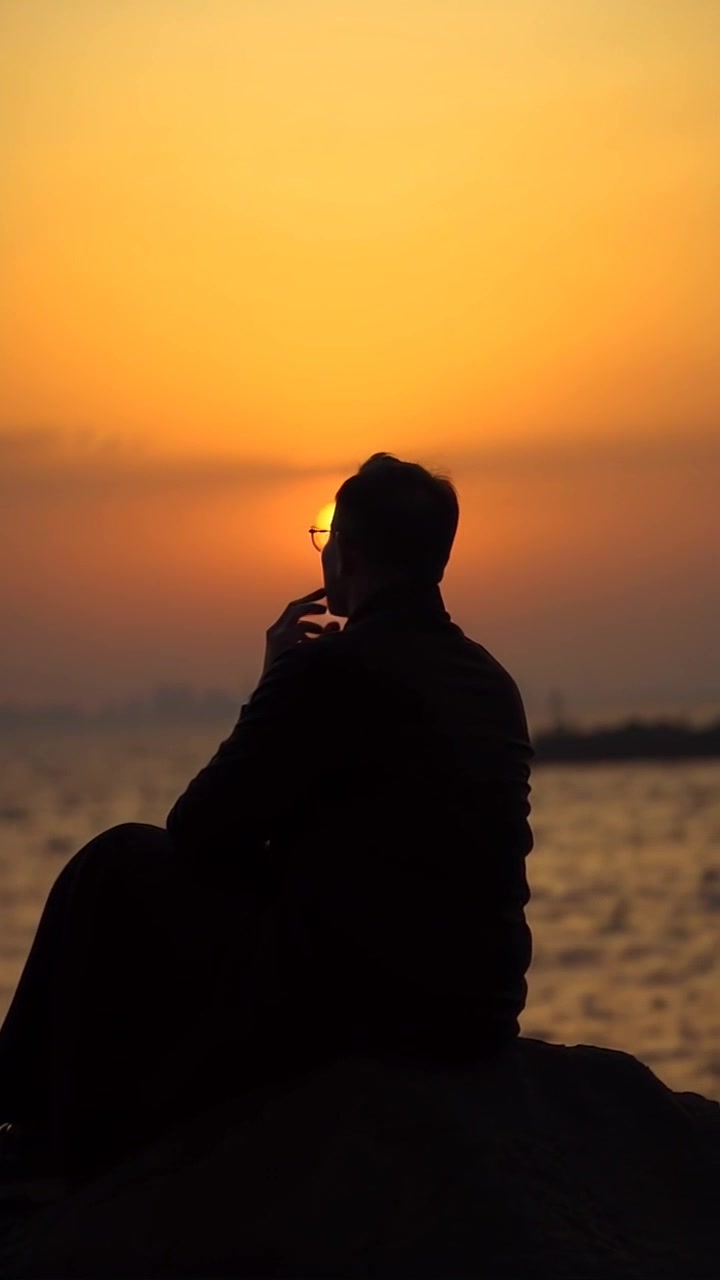 Subject: A contemplative figure sitting on a rock. Subject movement: The figure gazes steadily towards the horizon, reflecting a moment of introspection. Scene: A serene outdoor landscape, with rolling hills and an expansive sky at dusk. Style: Soft, warm twilight lighting creating a peaceful ambiance. Motion: A gentle panning shot that slowly reveals the surrounding panoramic view as the sun dips below the horizon, enhancing the atmosphere of calm and reflection.
