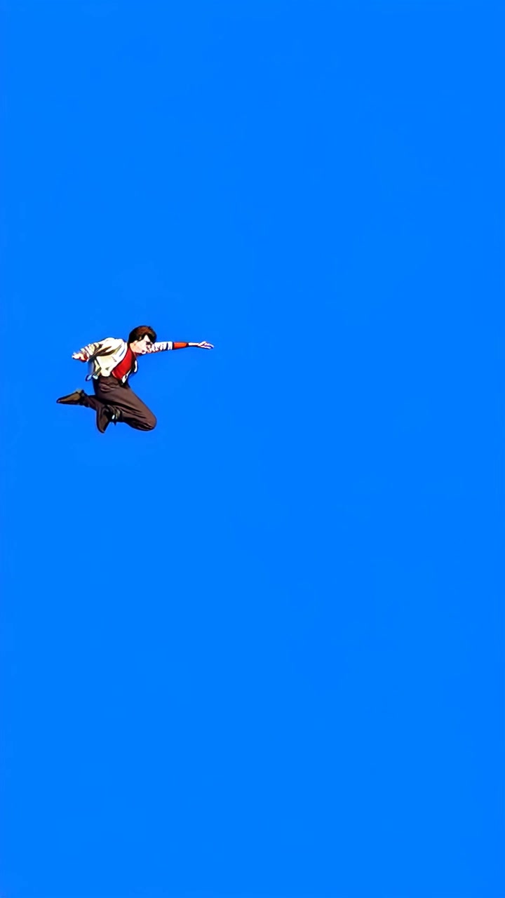 Subject: A daring individual leaping off a rooftop. Subject movement: Mateo is in mid-air, arms extended and face focused towards the ground below, creating a sense of urgency as he prepares to investigate a disturbance. Scene: Urban skyline setting, with a clear blue sky and surrounding buildings that emphasize the height of the jump. Style: Bright daylight, creating sharp contrasts with shadows on the rooftops. Motion: Camera follows Mateo with a dramatic panning shot, capturing the excitement of the leap as it tracks his descent, framing the cityscape in the background.