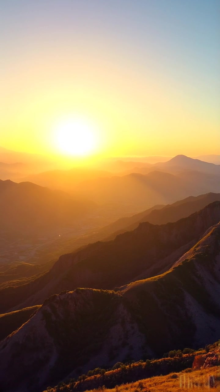 Subject: A figure standing on a mountain peak, arms raised in triumph. Subject movement: The figure holds their position, exuding a sense of victory and accomplishment. Scene: A breathtaking mountain peak overlooking an expansive landscape of valleys and distant ranges. Style: The golden glow of sunset pours over the scene, highlighting the rugged terrain and casting long shadows. Motion: Camera begins with a closeup on the figure's triumphant pose, then pulls back smoothly to reveal the stunning panorama, capturing the breadth of the landscape and the dramatic sky.