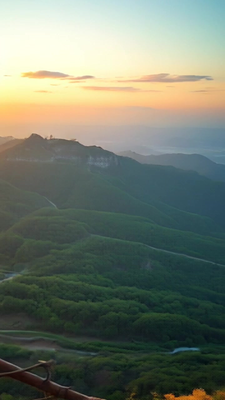 Scene: A breathtaking view of a valley from a cliff edge at sunset, with vivid colors painted across the sky. Style: Warm sunset lighting casting golden hues over the landscape, enhancing the beauty of the rugged terrain below. Motion: Camera pans slowly across the cliff, revealing the expansive valley bathed in soft, ambient light as the sun dips below the horizon.