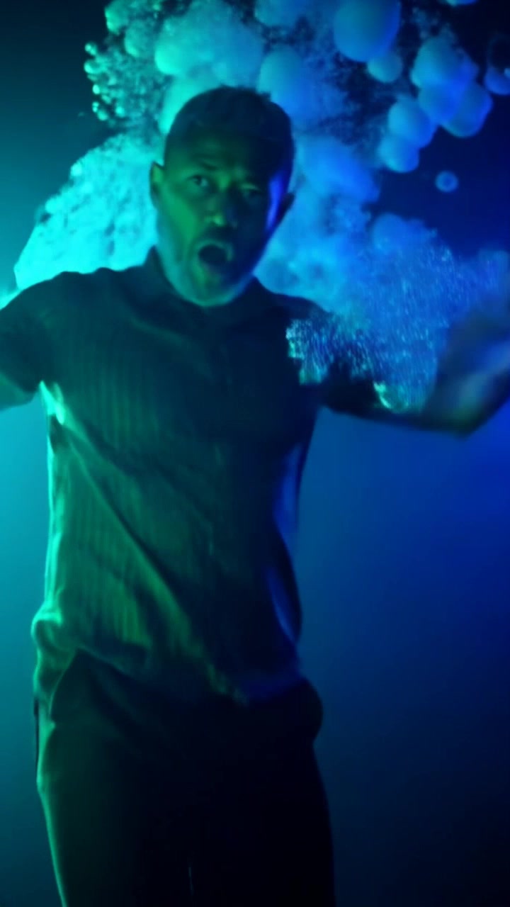 Subject: A young man in distress underwater, bubbles rising around him. Subject movement: He is thrashing his arms and legs, struggling to push towards the surface. Scene: A dramatic underwater environment filled with swirling currents and beams of light filtering through the water. Style: Soft blue light creating an ethereal atmosphere, with a sense of urgency and tension. Motion: The camera slowly pans upward as the subject flails, capturing the bubbles escaping his lips, and then circles around to showcase his expressions of panic.