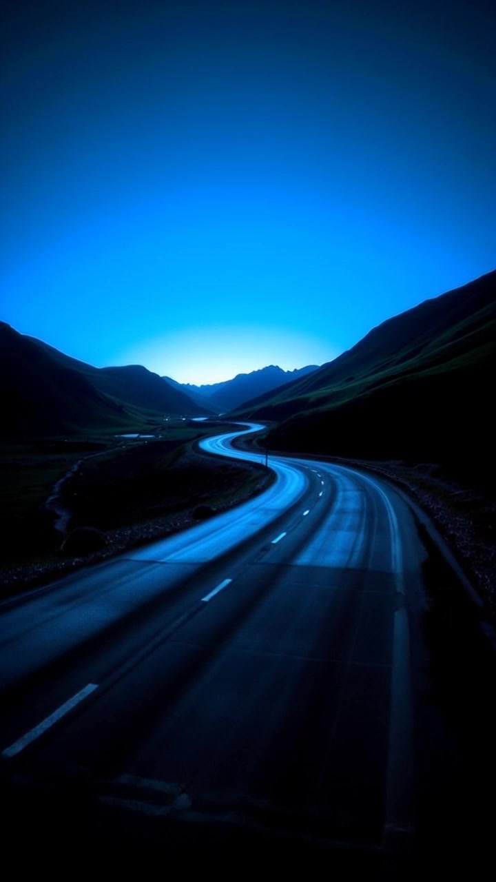Scene: A winding road meandering through a picturesque landscape, flanked by lush green hills under a clear blue sky. Style: Bright, inviting daylight illuminating the vibrant colors of the hills and the road. Motion: Camera follows the contours of the road, sweeping gently from a drone's perspective, creating a sense of journey as it reveals the stunning scenery at every turn.