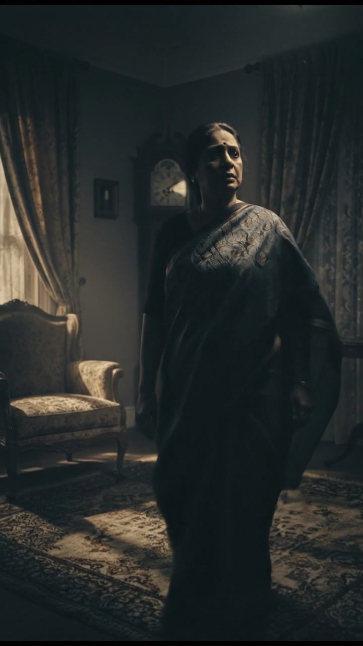 Mrs. Singh looking worried, glancing around the dimly lit living room.