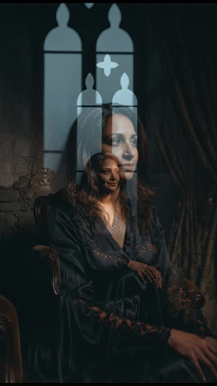 Asha sitting alone in a dimly lit room, staring thoughtfully at a window.