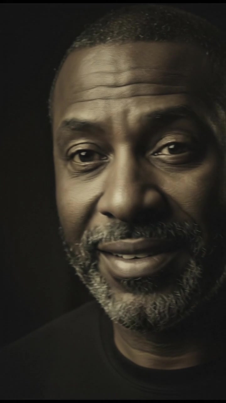 A close-up of Kwame's face, showing his dark gray beard and furrowed features, as if listening attentively.