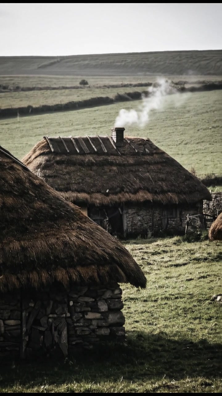 A view of a small village with thatched-roof houses amid green fields.