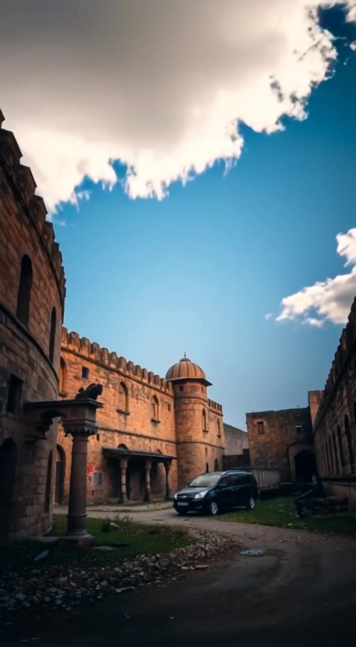 Clouds drift lazily across a clear blue sky above the ancient architecture of Bhangarh Fort in Rajasthan.